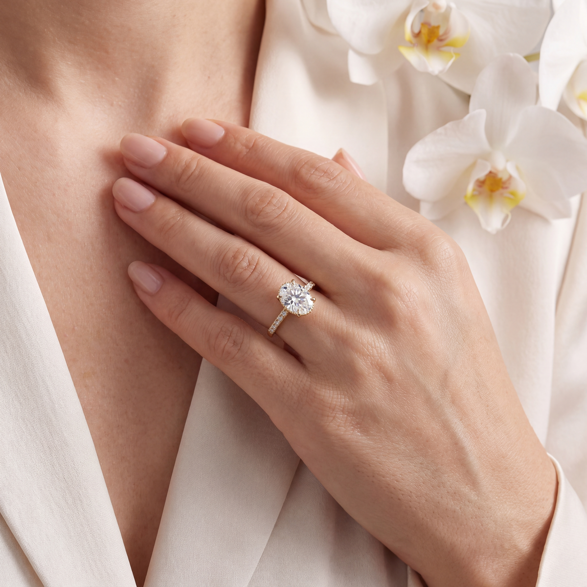 Close-up lifestyle shot of a woman wearing the yellow gold oval moissanite ring against a white outfit.