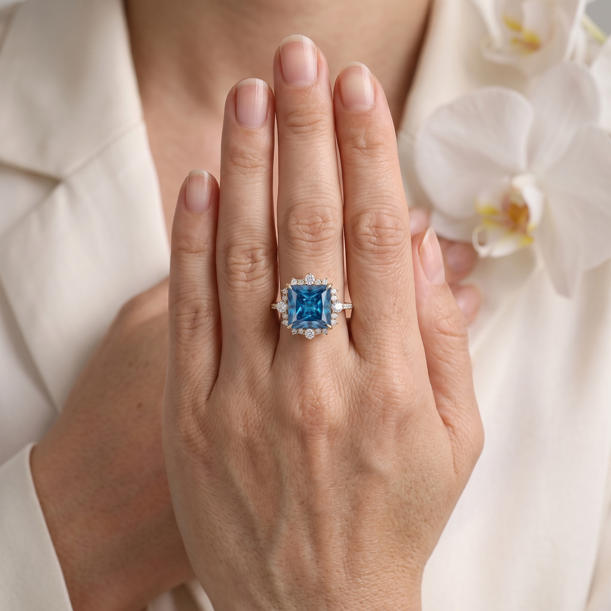 Model showcasing a rose gold princess-cut blue moissanite halo ring resting against white attire.