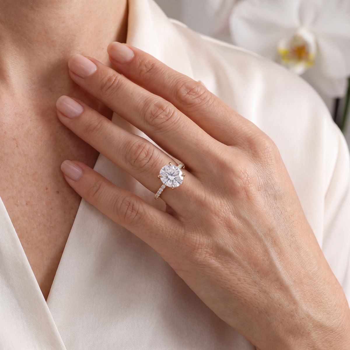 Model wearing a yellow gold east-west oval moissanite engagement ring against white silk.