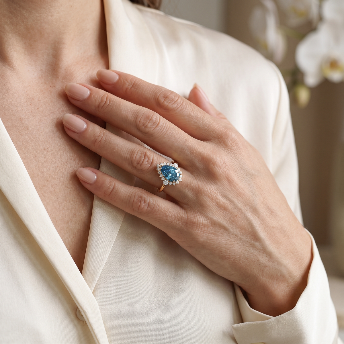 Close-up of a pear-cut blue moissanite halo ring in rose gold worn on a model's hand.