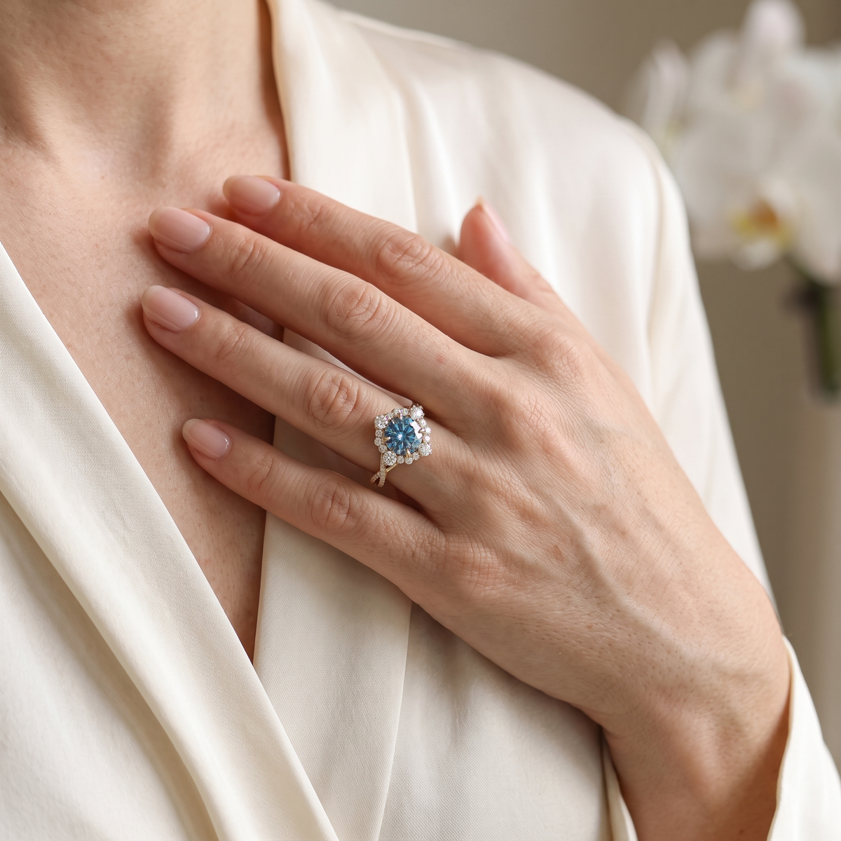 A woman wearing the rose gold blue moissanite halo engagement ring resting her hand gently against her silk outfit.