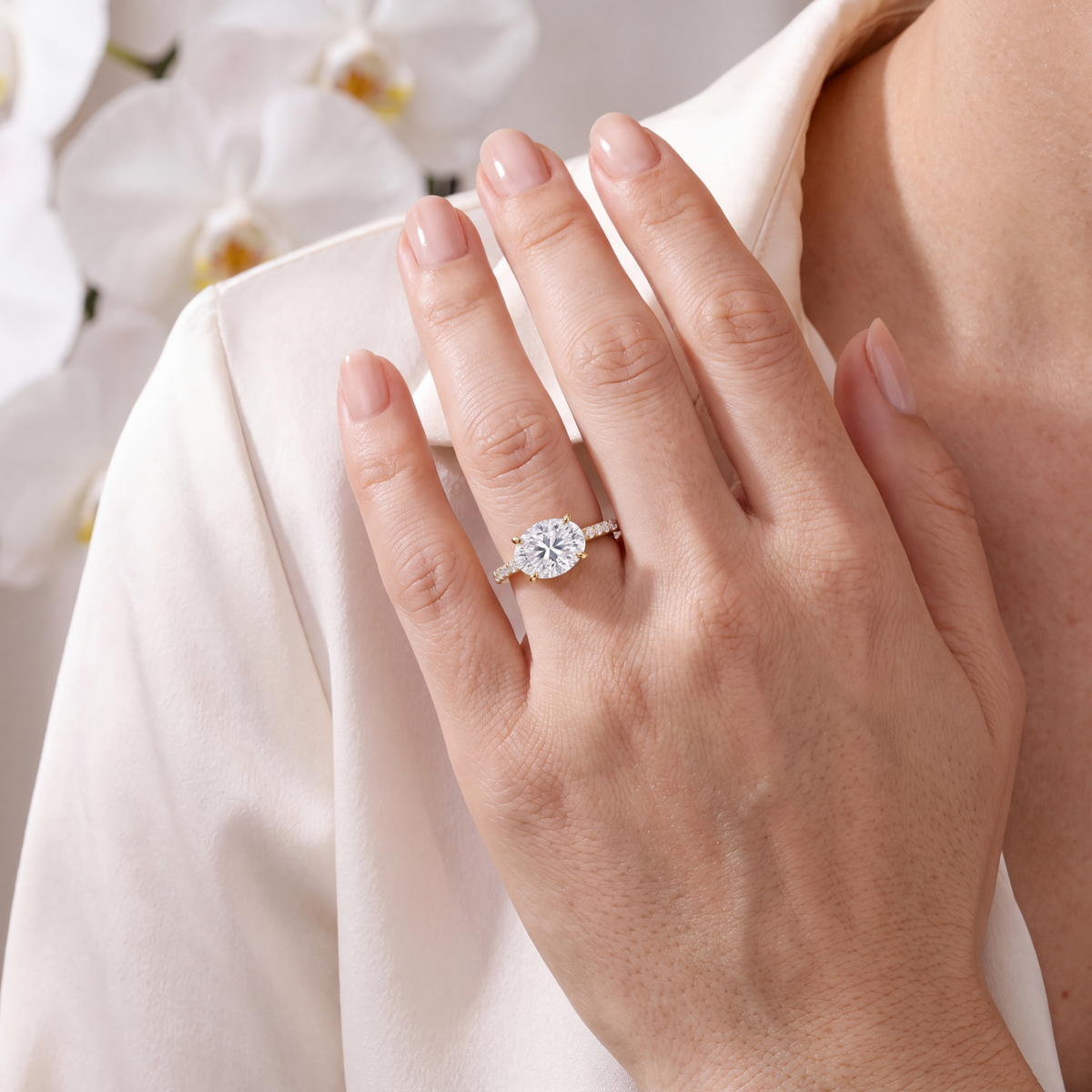 Close-up of a hand resting on a shoulder featuring an east-west oval moissanite engagement ring in yellow gold.
