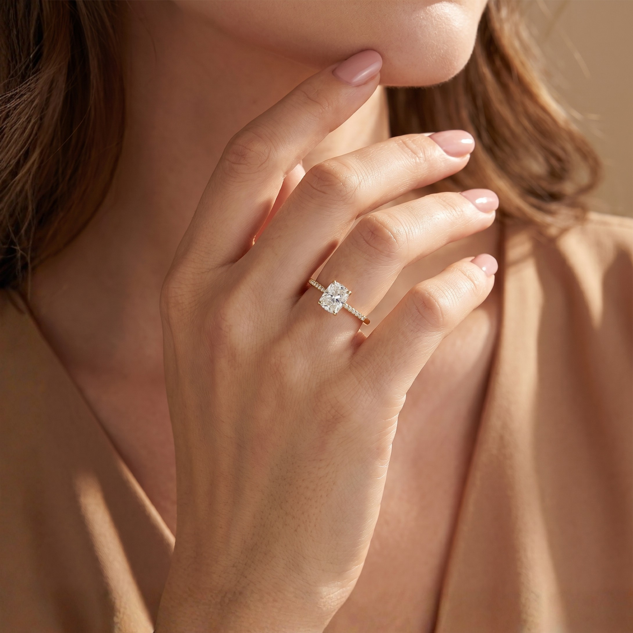 A closeup of a hand displaying a beautiful yellow gold cushion cut moissanite engagement ring with a pavé band.
