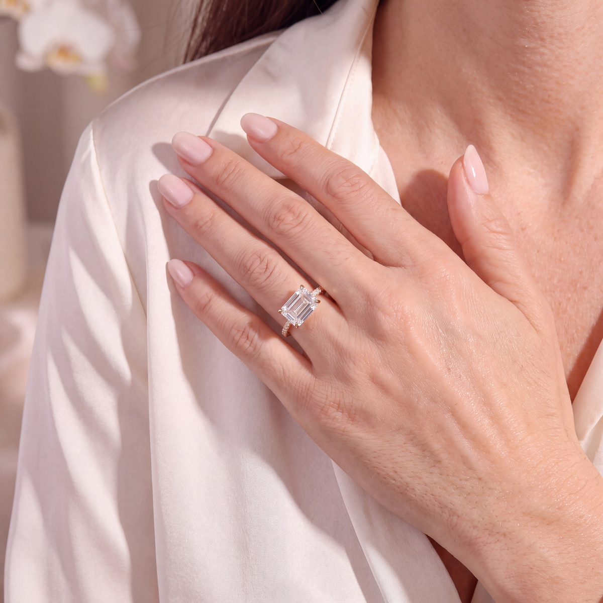 Model wearing a yellow gold east-west emerald-cut moissanite ring against a silk blouse.