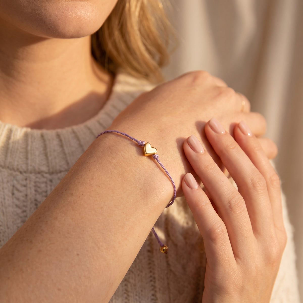 Lavender cord bracelet with gold-tone heart worn on a wrist