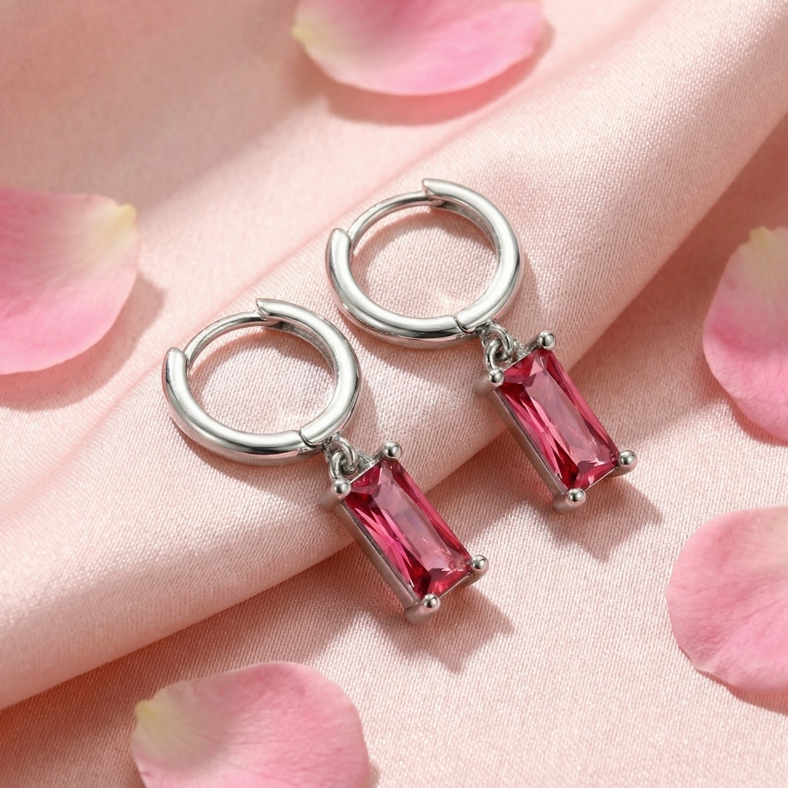 Silver emerald-cut pink tourmaline drop hoop earrings displayed on pink fabric with scattered rose petals.