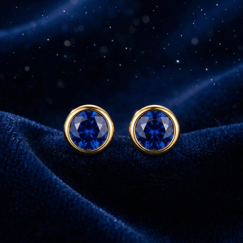 Front view of round simulated sapphire bezel stud earrings in 18K gold vermeil on blue velvet.