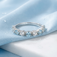 Round cut simulated aquamarine half-eternity band ring in solid gold on blue fabric and white marble.