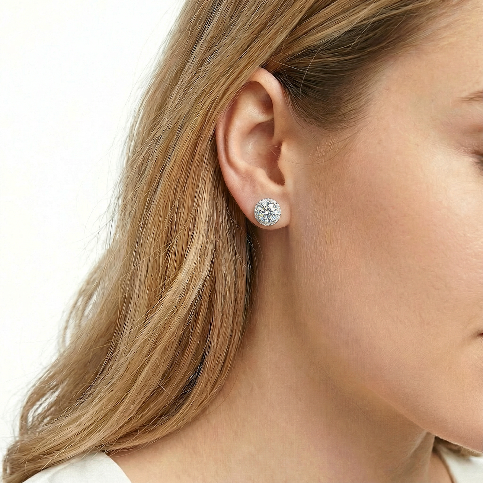 Side view of a round cut zirconia halo stud earring in sterling silver worn on a woman's ear.
