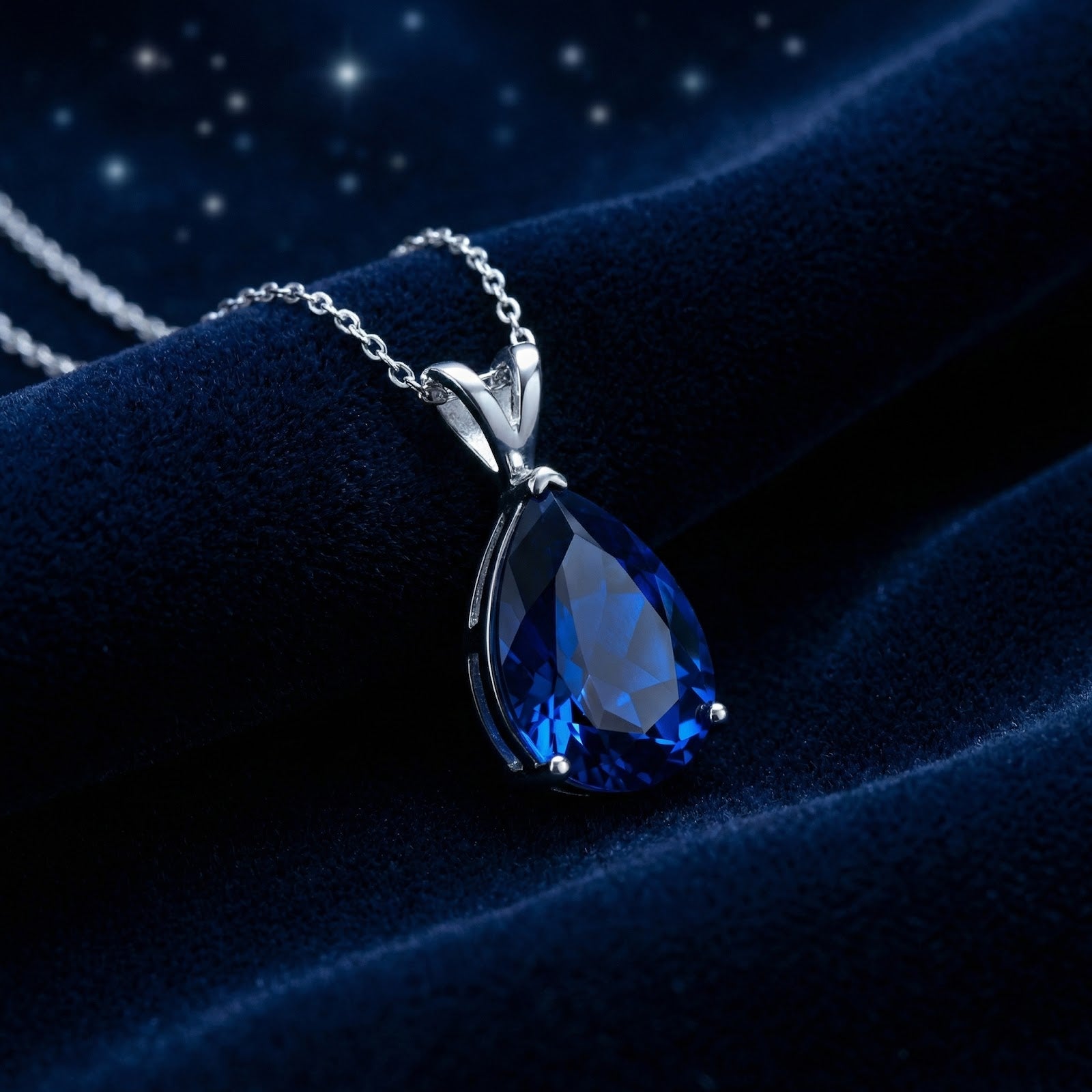 Pear cut royal blue simulated sapphire pendant in sterling silver on a dark blue velvet fabric background.