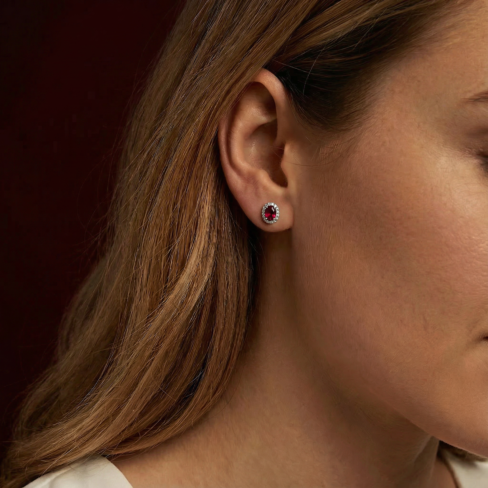 Side profile of a woman wearing an oval simulated ruby halo stud earring in sterling silver.