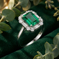 Octagon cut simulated emerald ring in solid gold with a halo setting on green velvet with eucalyptus leaves.