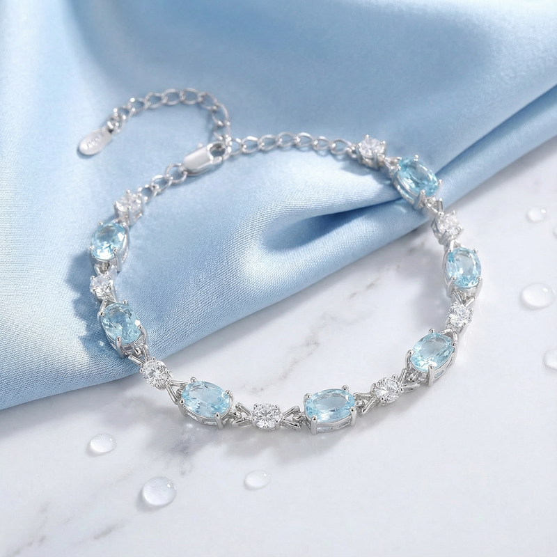 Close-up of the Melodia silver bracelet featuring oval cut light blue simulated aquamarine stones on blue silk.