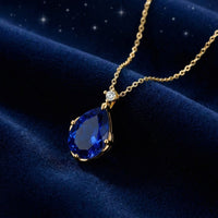 Pear-cut simulated sapphire necklace in 18K gold vermeil resting on deep blue velvet fabric.