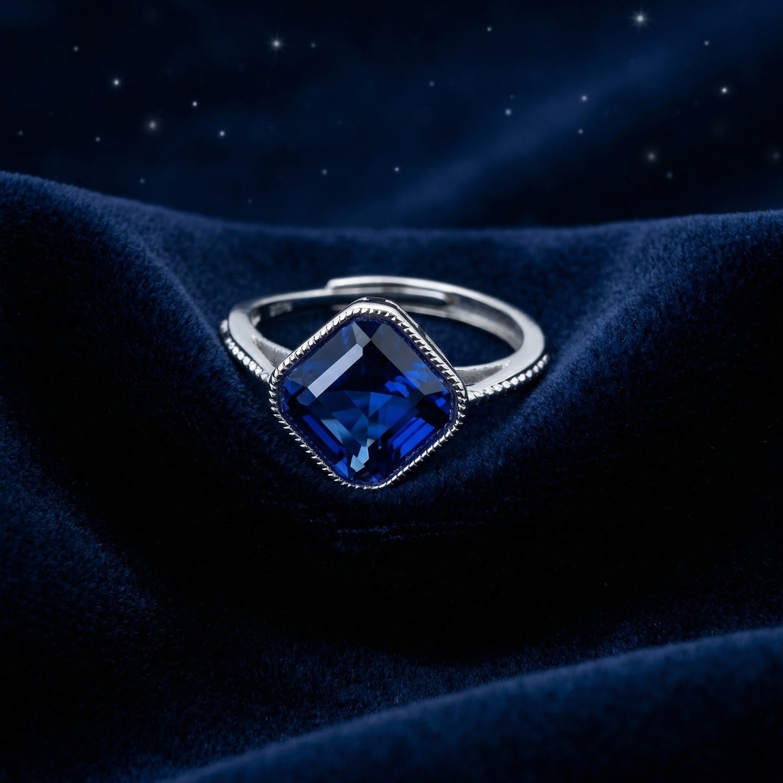 Cushion-cut simulated sapphire ring in S925 sterling silver on dark blue velvet with a starry background.