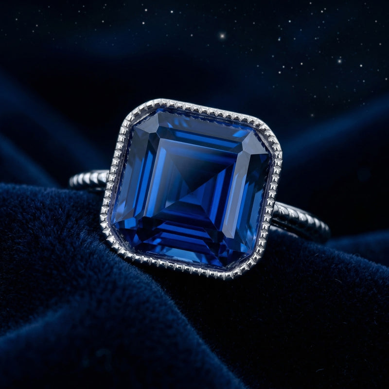 Close-up of a cushion-cut blue simulated sapphire in a milgrain sterling silver setting on blue velvet.
