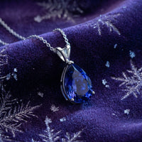 Pear-cut blue moissanite necklace in S925 sterling silver resting on purple velvet with snowflake patterns.
