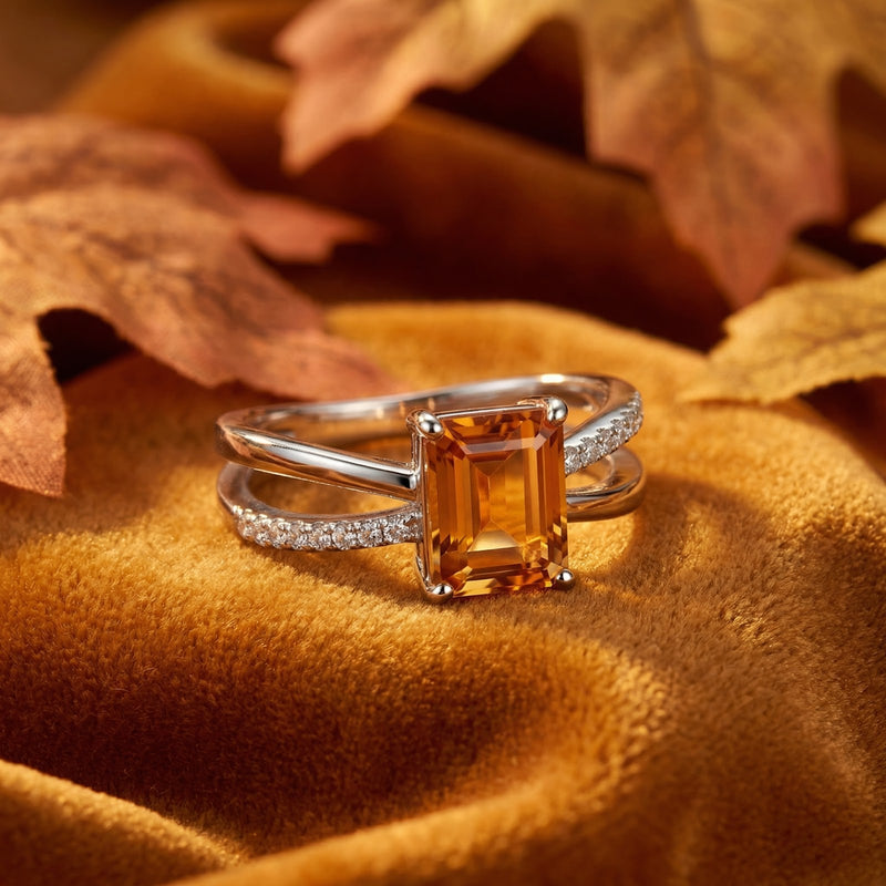 Angled view of the Evelisse sterling silver twist ring with a honeyed radiant-cut topaz on velvet with leaves.