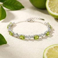 Station bracelet with oval simulated peridot and round clear stones on a lifestyle background in solid gold.