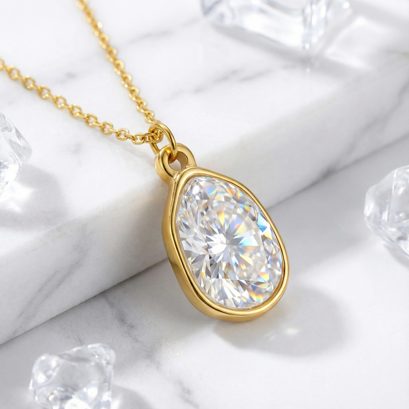 Gold-finished stainless steel necklace with a pear-cut zirconia pendant on a marble surface with crystal accents.