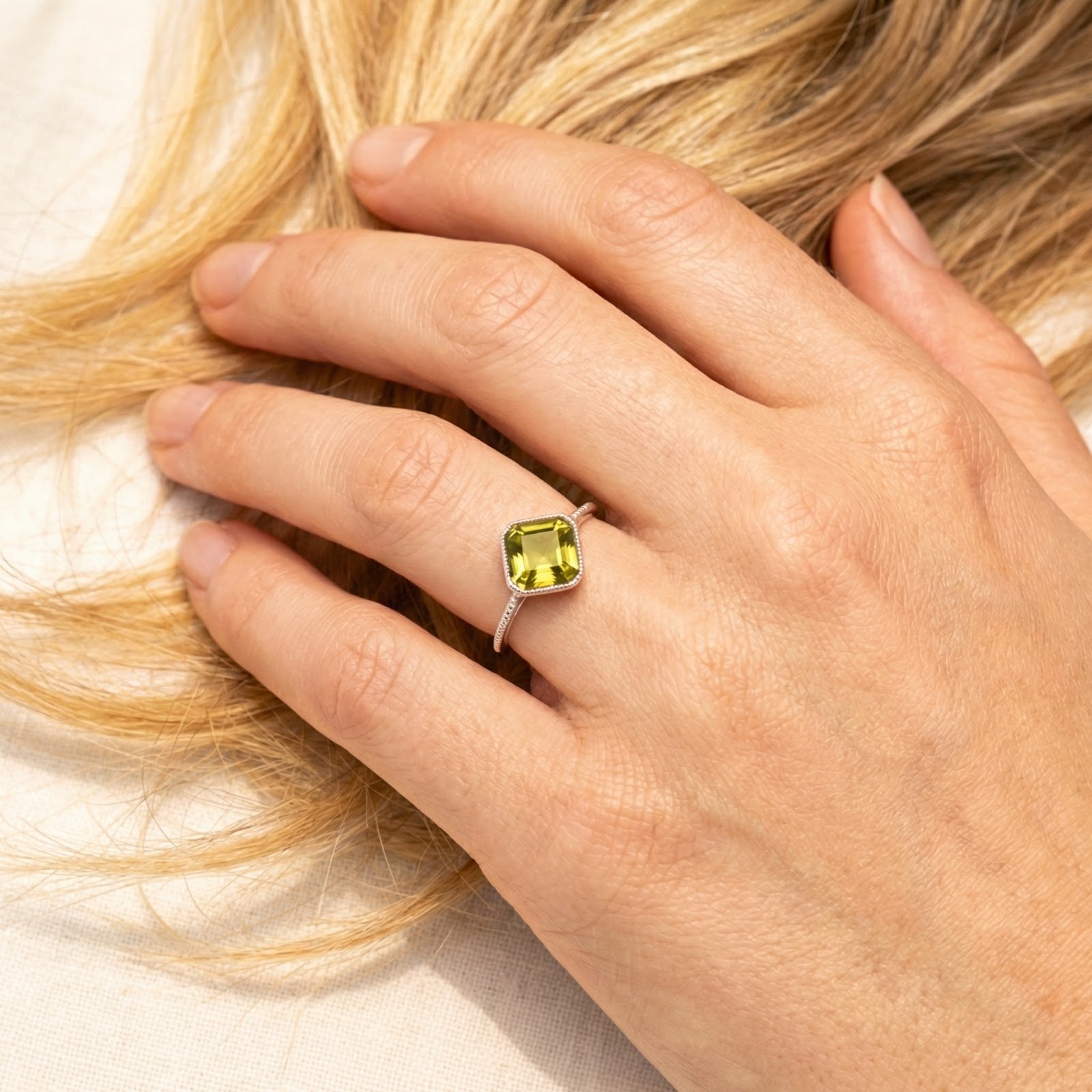 Close-up of a hand wearing the square-cut simulated peridot sterling silver ring against blonde hair.