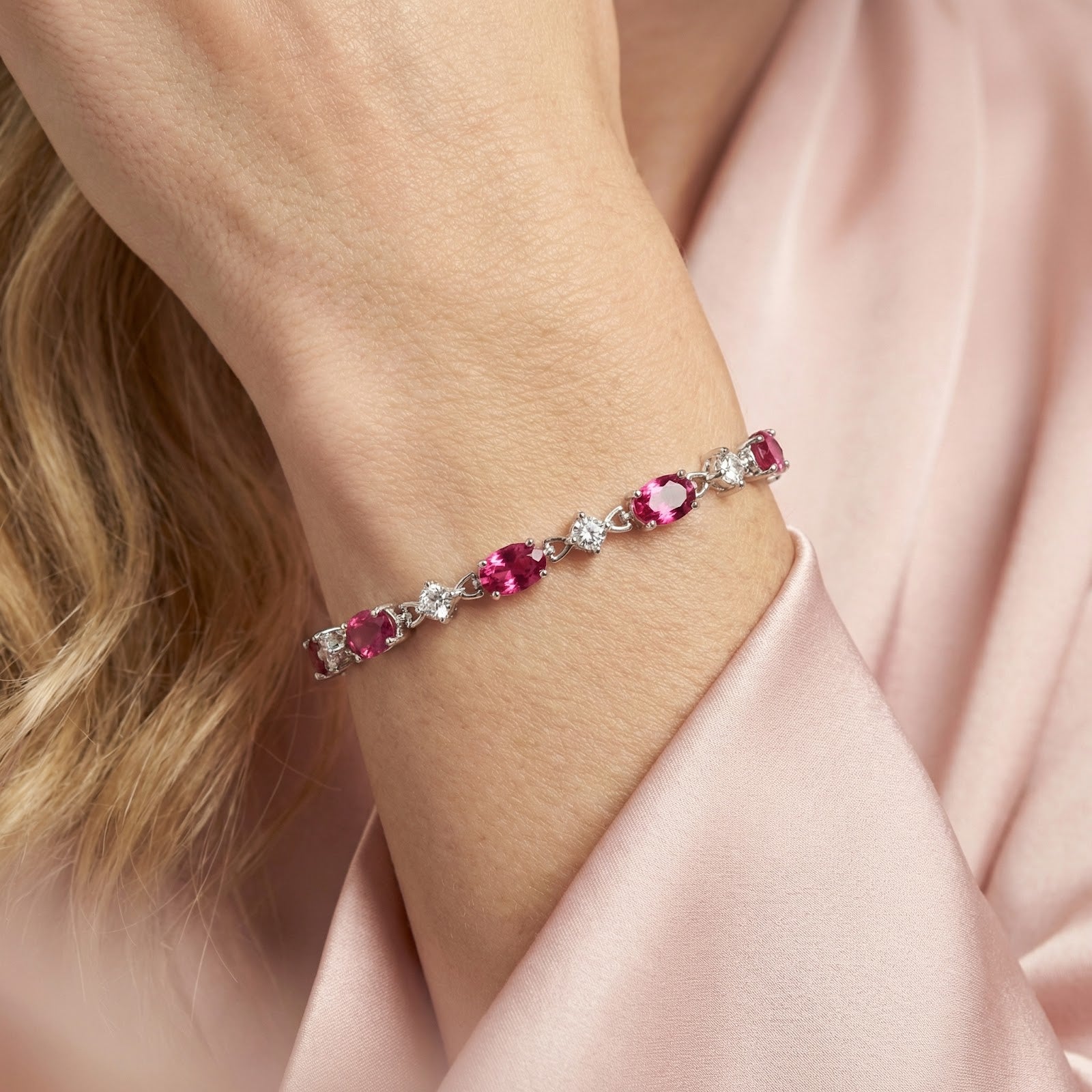Close-up of oval pink tourmaline stones in a sterling silver tennis bracelet setting worn on the wrist.