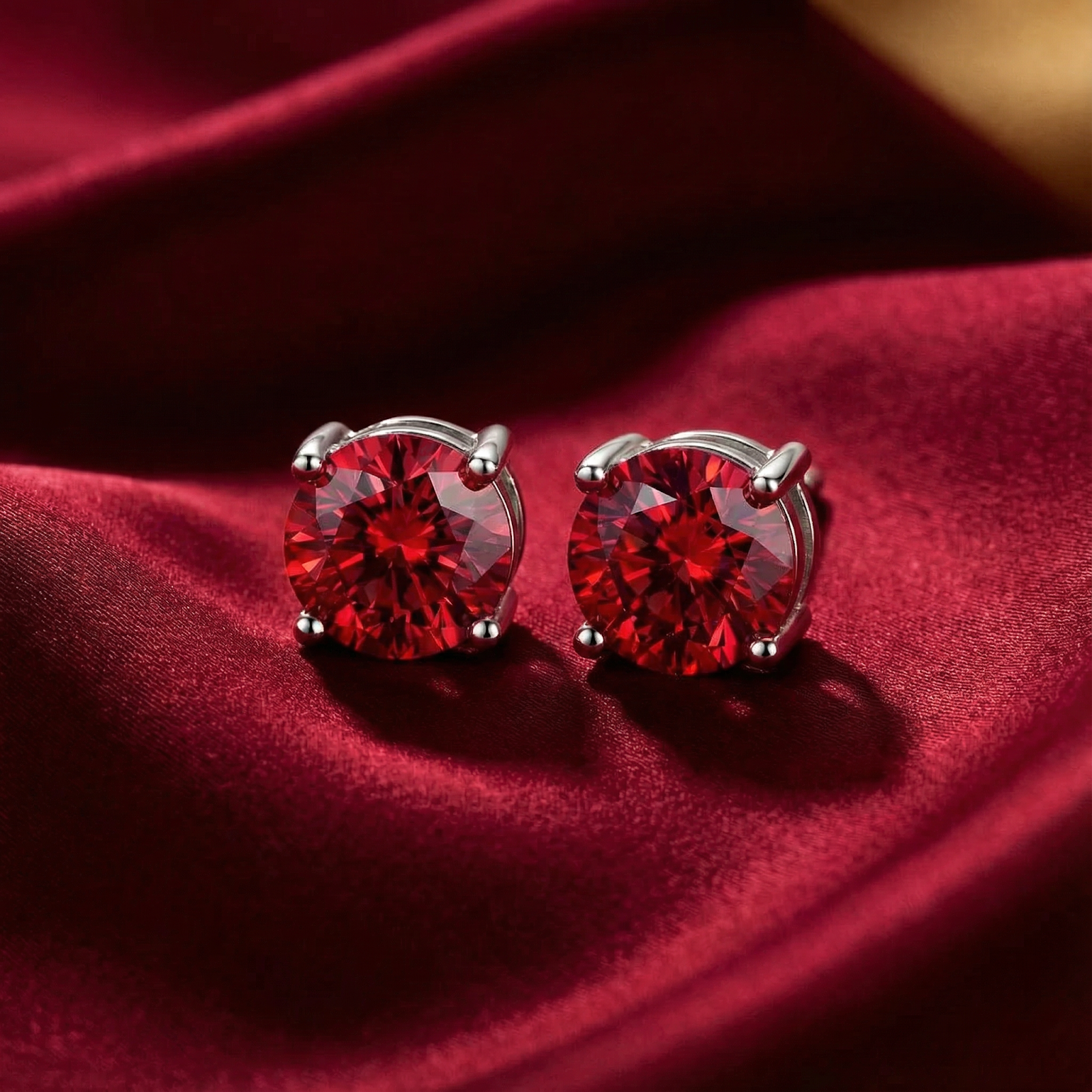 Round cut simulated ruby stud earrings in sterling silver settings on a red silk background.