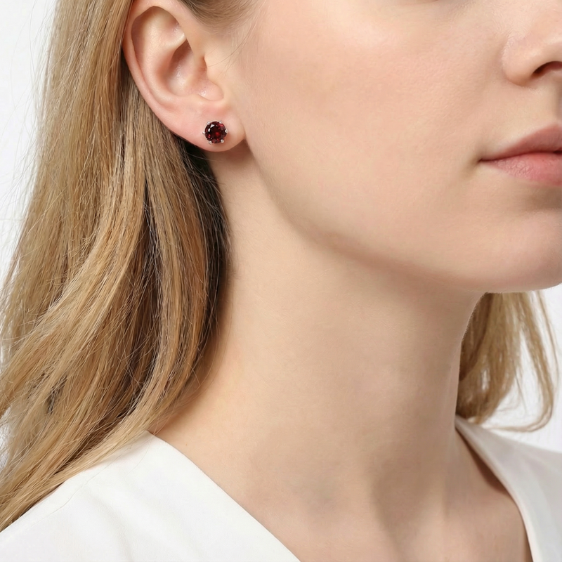 Woman wearing a round red garnet stud earring in sterling silver on her earlobe.