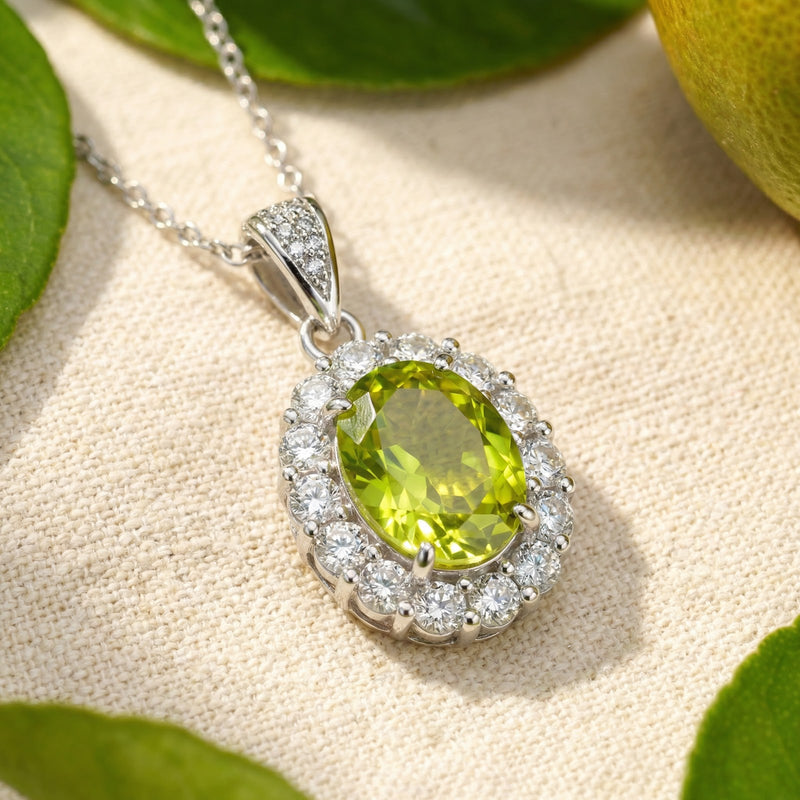 Lifestyle shot of the sterling silver oval peridot halo necklace on fabric with fresh lime slices and leaves.