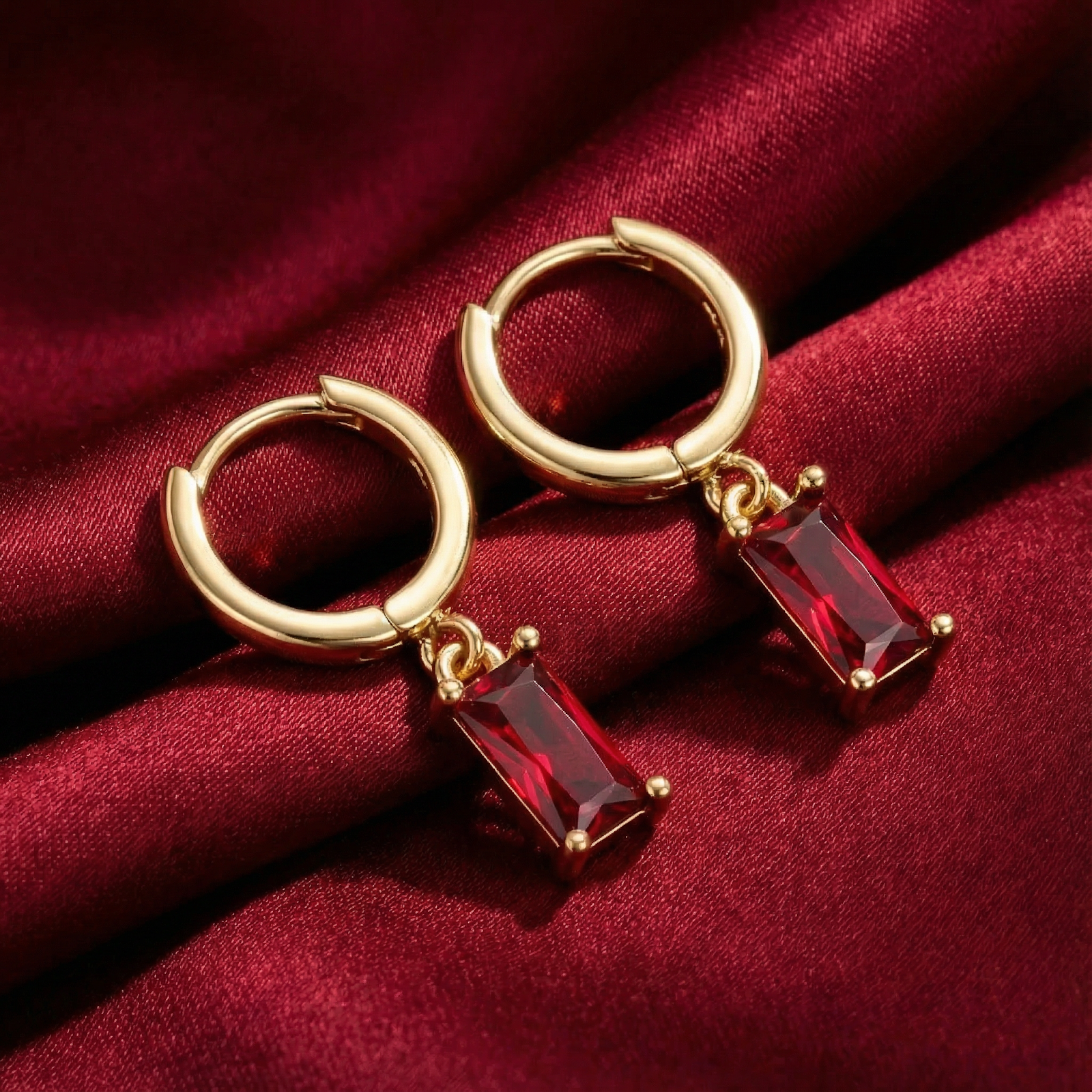 18K gold vermeil hoop earrings with emerald-cut simulated ruby drops on red silk fabric.