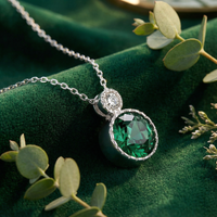 Round-cut simulated emerald drop necklace in sterling silver on green velvet with eucalyptus leaves.