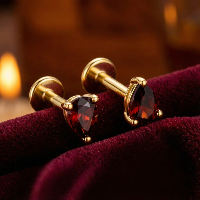 Close-up of pear cut simulated garnet stud earrings in 18K gold vermeil showing stone facets on red velvet.