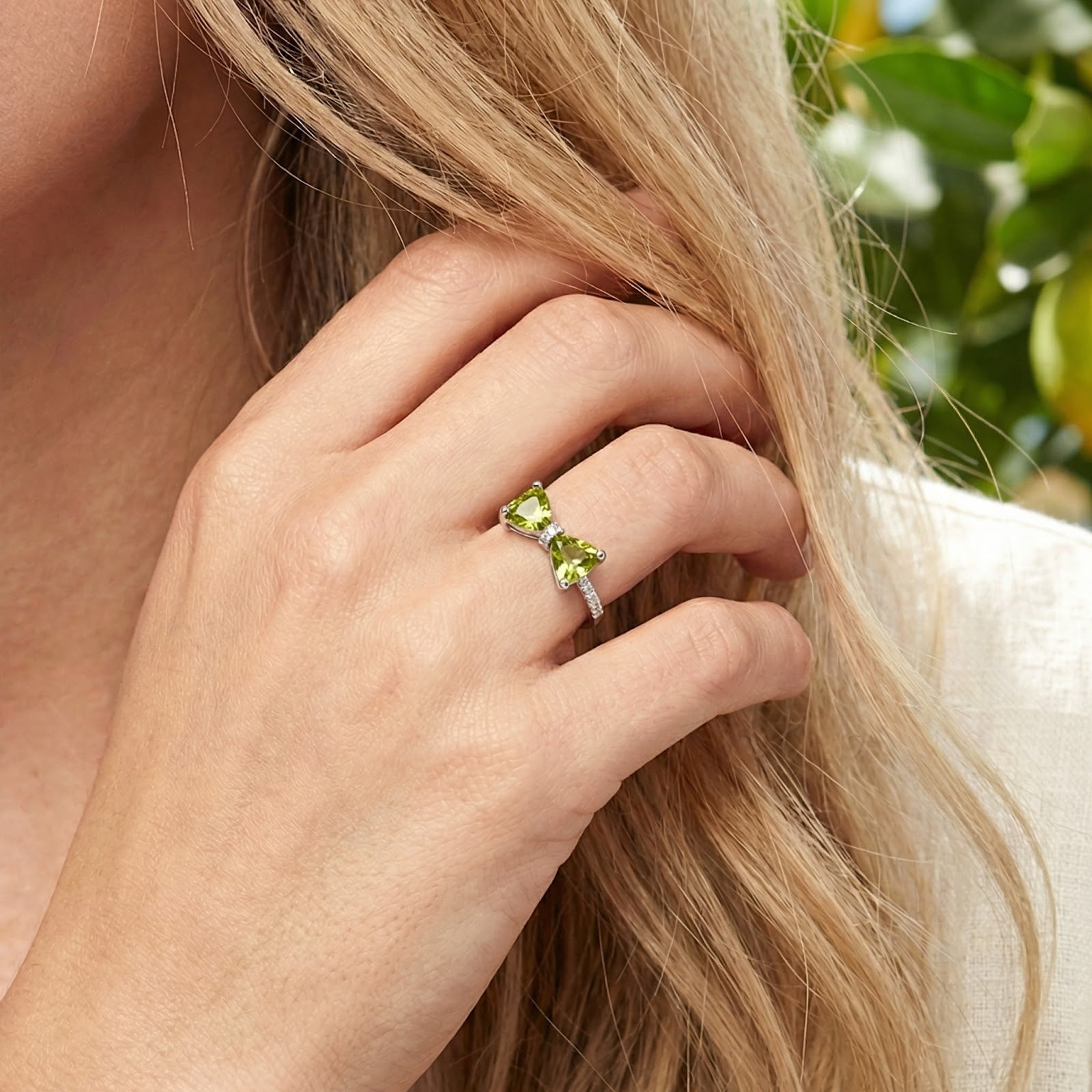 Sterling silver bow ring with trillion-cut green simulated peridots worn on a woman's hand.