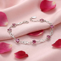 Solid gold station bracelet with round simulated pink tourmaline stones on pink silk with rose petals.