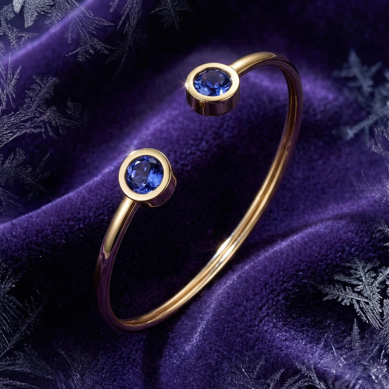 Gold stainless steel Veralis cuff featuring round blue simulated tanzanite stones on purple velvet.
