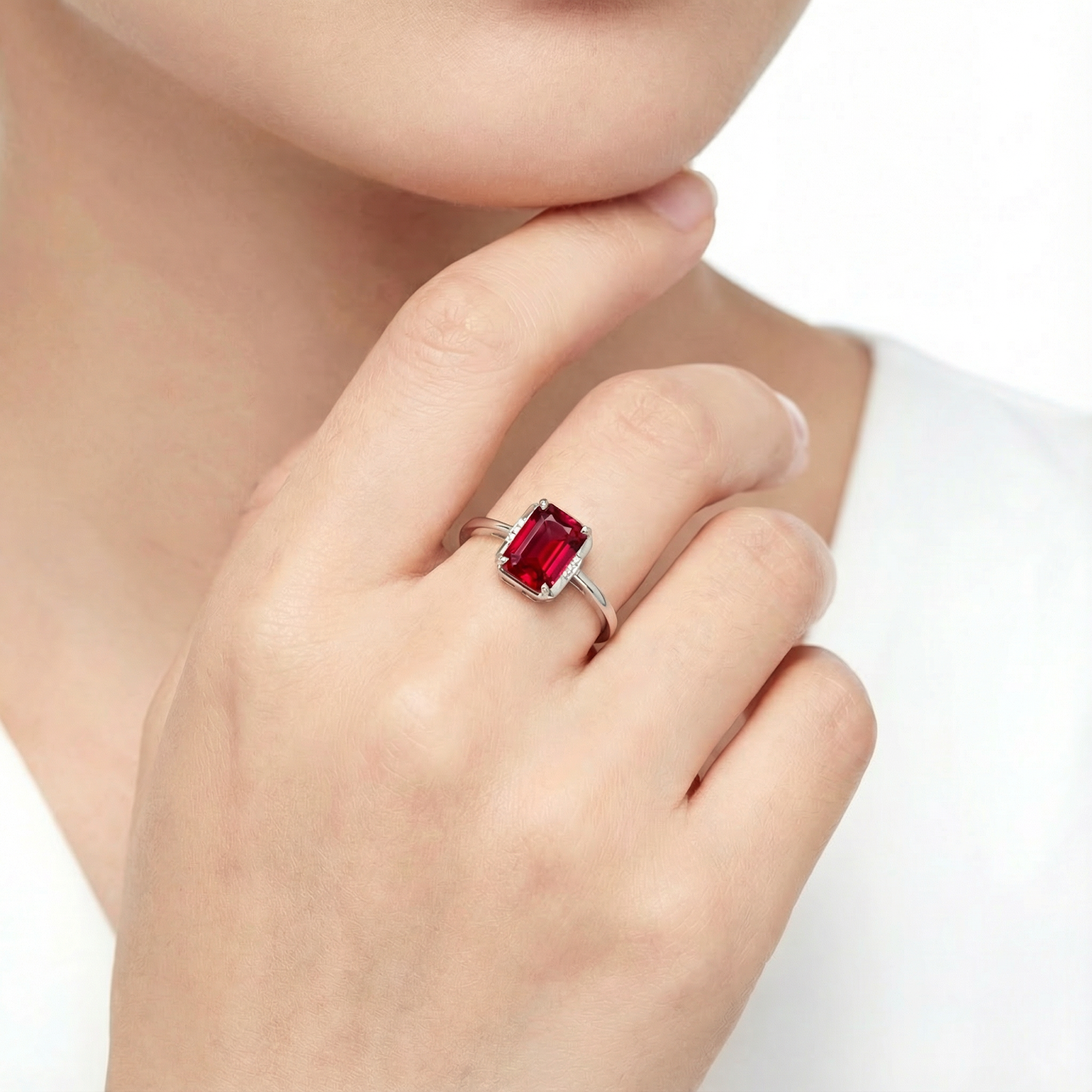 Emerald cut simulated ruby sterling silver ring worn on a woman's finger against a white background.
