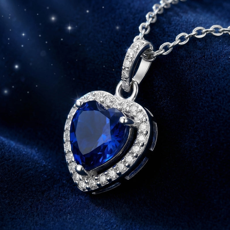 Side-angled macro of the heart-shaped simulated sapphire pendant and sterling silver halo setting on blue velvet.