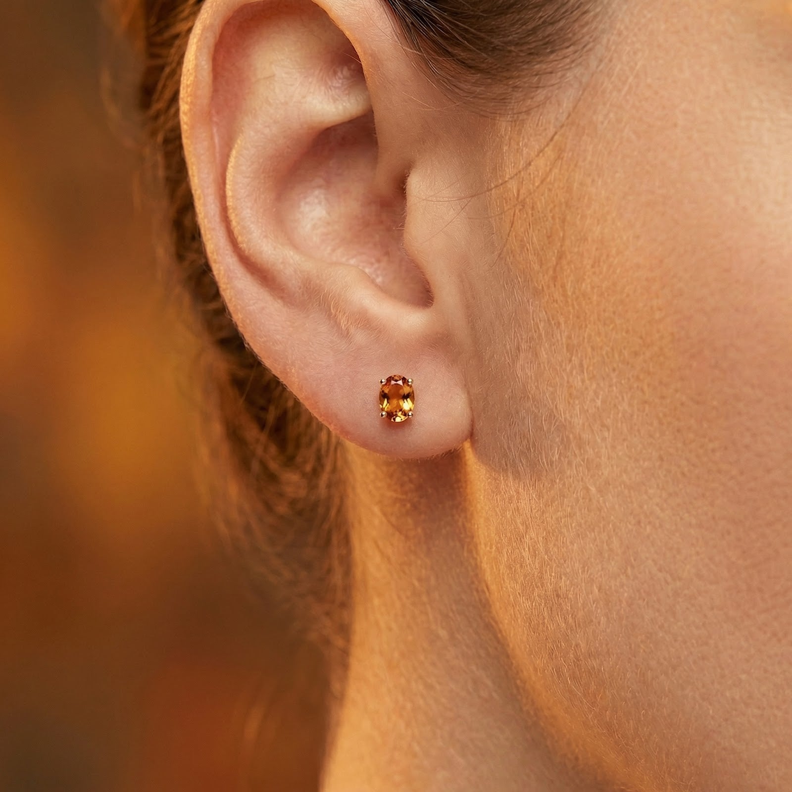 Close-up of an oval simulated topaz stud earring in 18K gold vermeil worn on a model's ear.