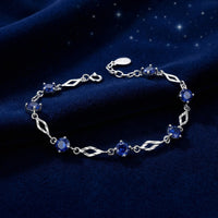 Solid gold station bracelet with round blue simulated sapphires resting on blue velvet.
