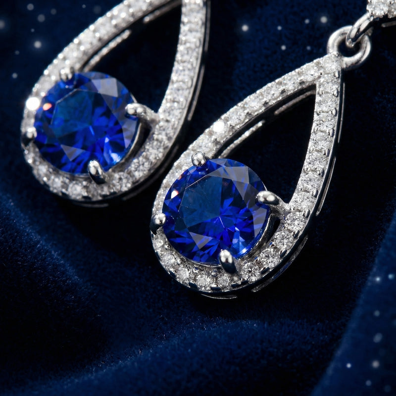 Close-up of round-cut simulated sapphire stones set in sterling silver teardrop halo earrings.