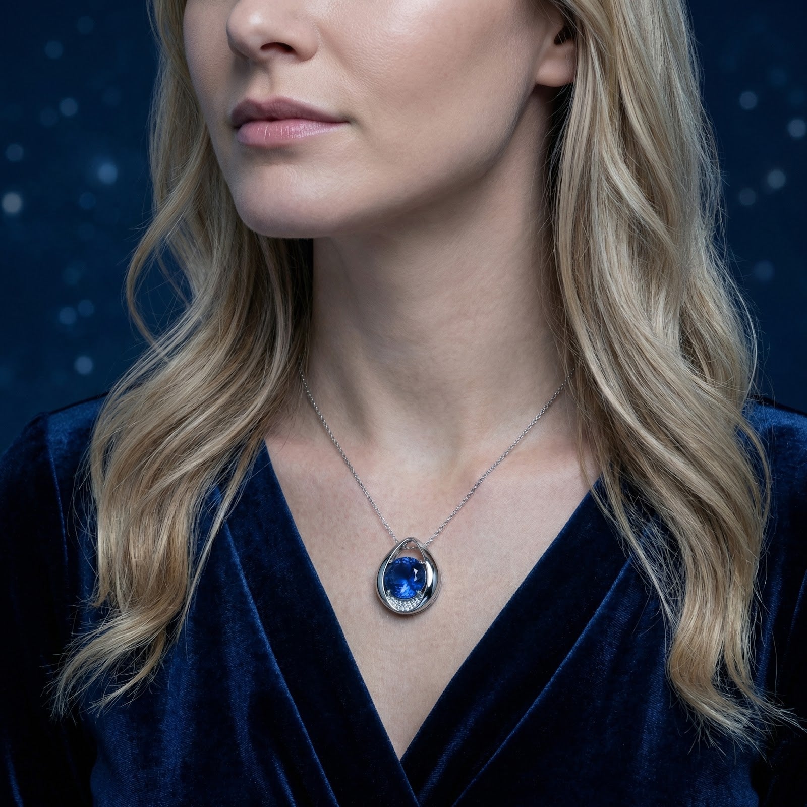 Model wearing the royal blue sapphire teardrop necklace in sterling silver against a dark background.