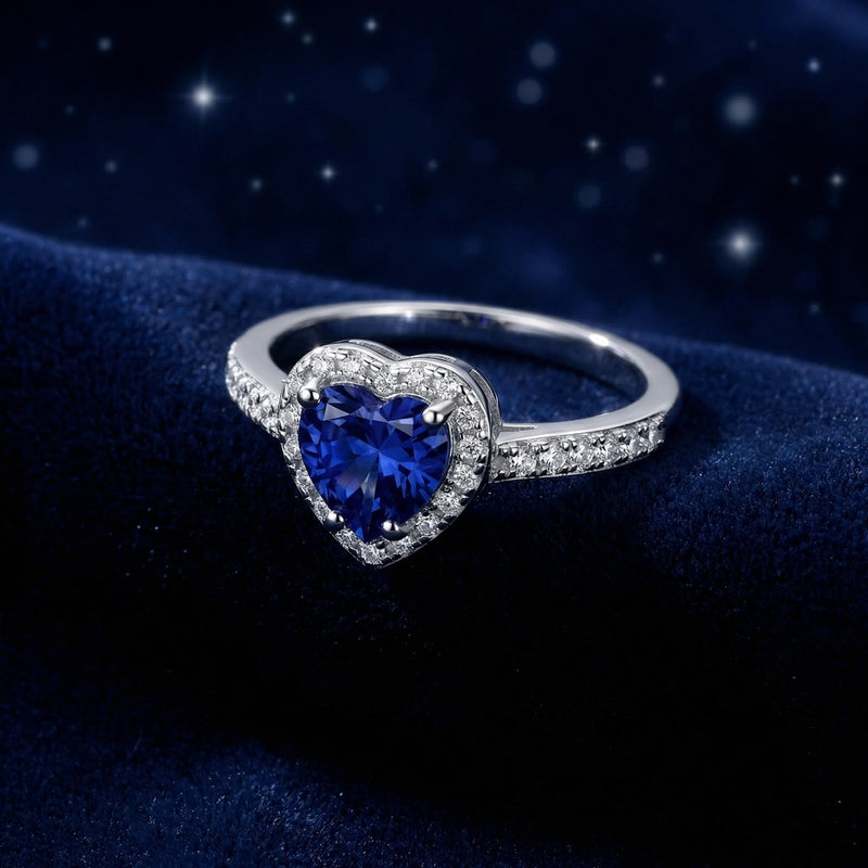 Angled view of the heart-shaped blue sapphire sterling silver ring with a pavé band on a velvet background.