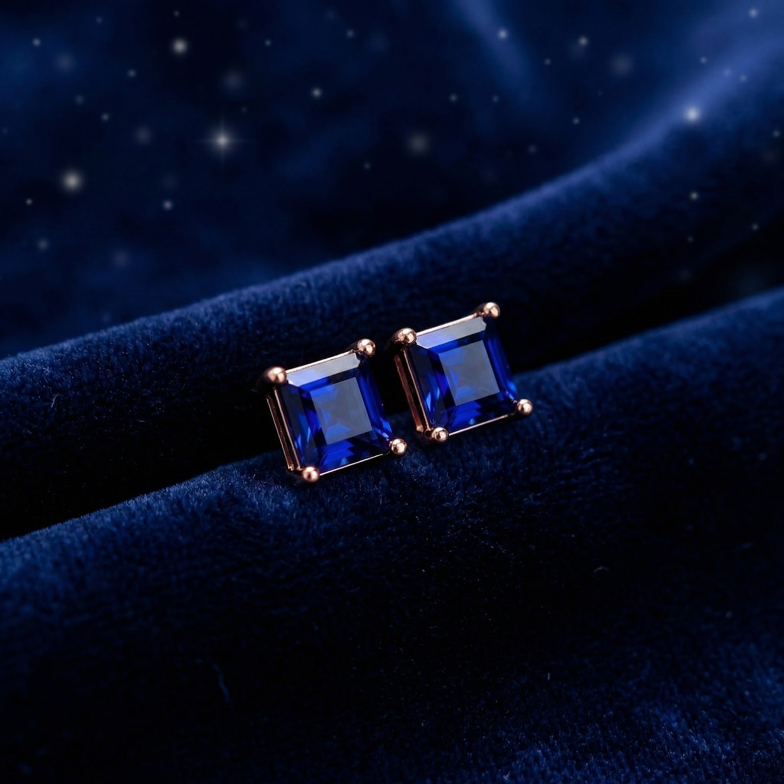 Square simulated sapphire stud earrings in 18K rose gold vermeil on a dark blue velvet background.