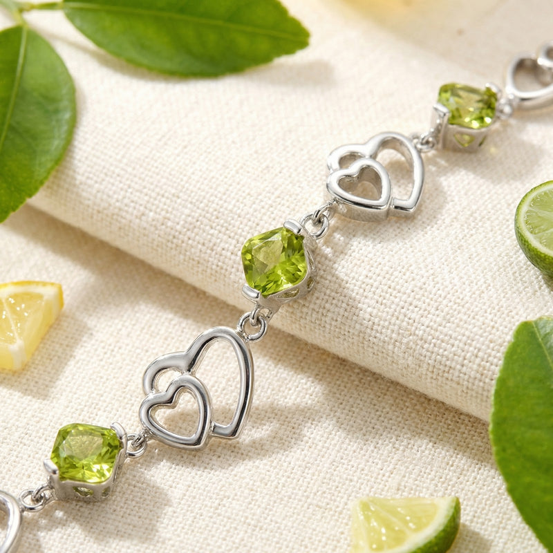 Close-up of sterling silver heart links and square-cut simulated peridot stones on the Perisella heart bracelet.