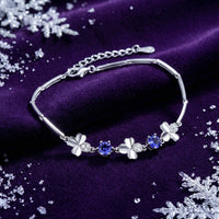 Silver clover bracelet with round blue simulated tanzanite stones on purple velvet with snowflakes.