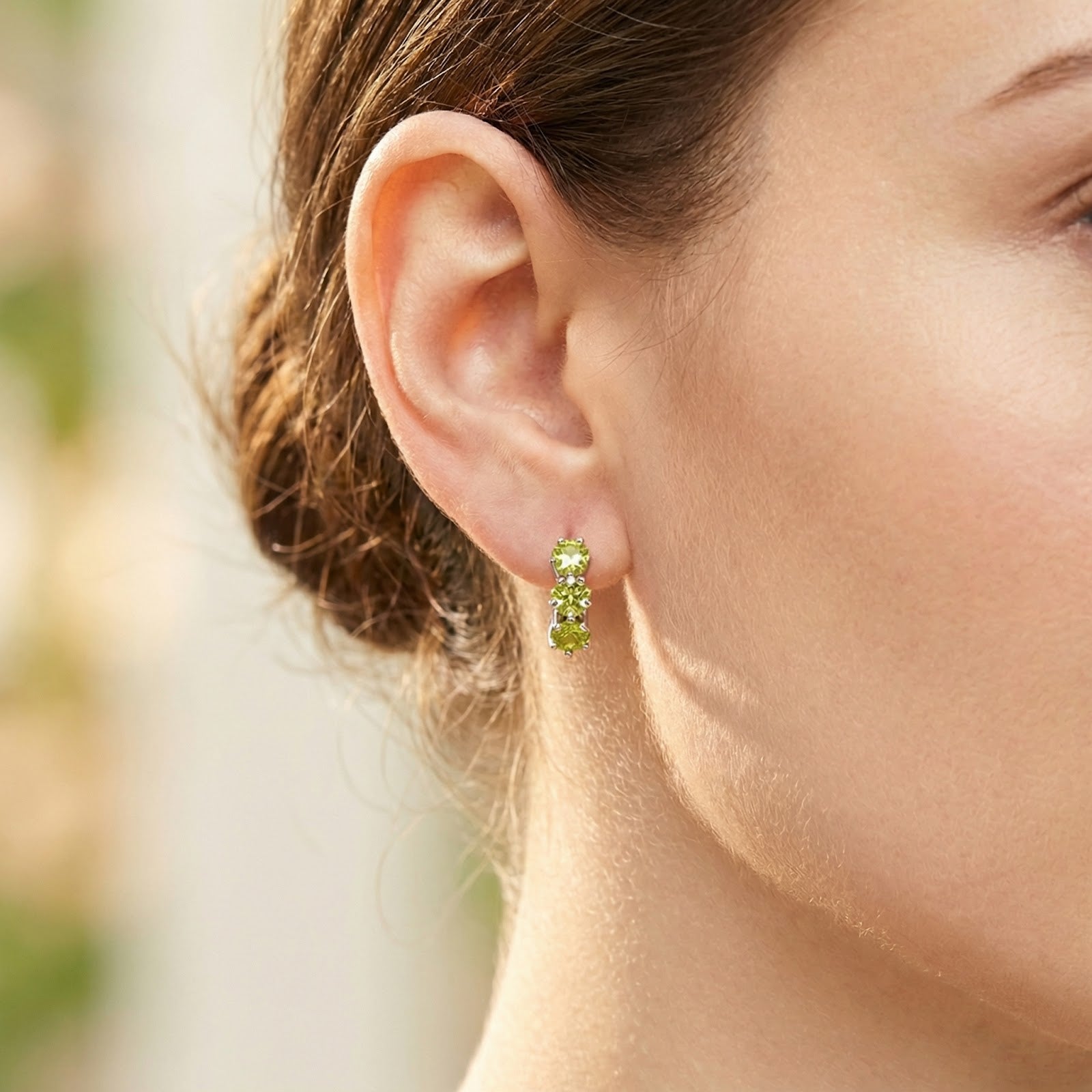 Close-up of a woman's ear wearing a sterling silver hoop earring with three star-cut green peridot stones.