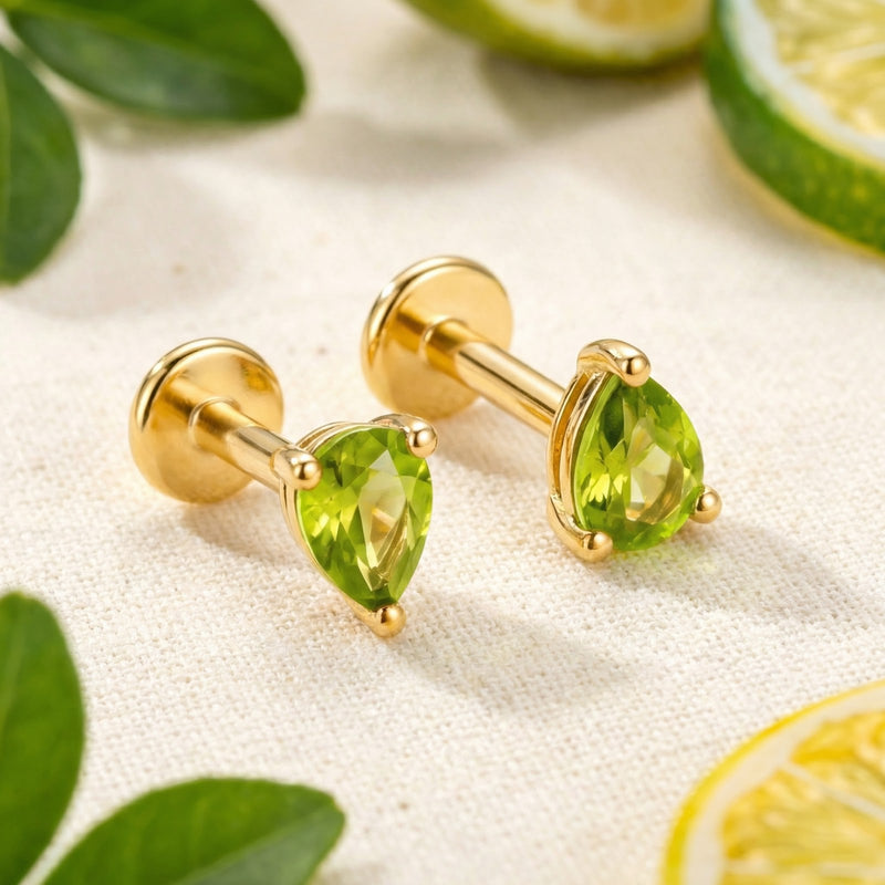 Pair of 18K gold vermeil pear-cut simulated peridot stud earrings displayed on a neutral fabric with lime slices.