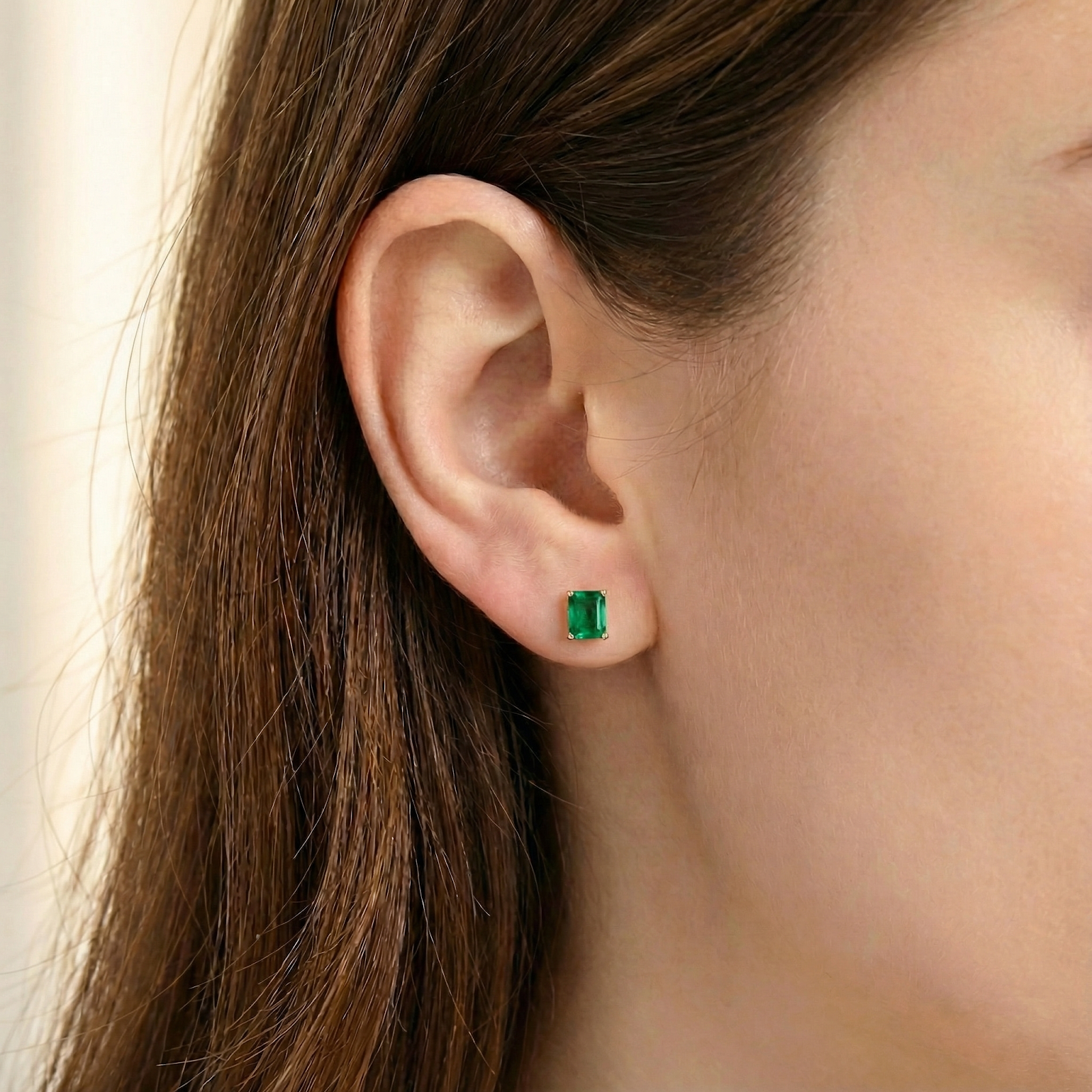 Emerald cut simulated emerald stud earring in 18K gold vermeil worn on a woman's ear.