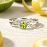 Zelinda bypass ring in solid gold with a round simulated peridot on a textured lifestyle background.
