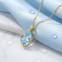 Pear cut simulated aquamarine pendant in 18K gold vermeil on a light blue fabric background with water droplets.